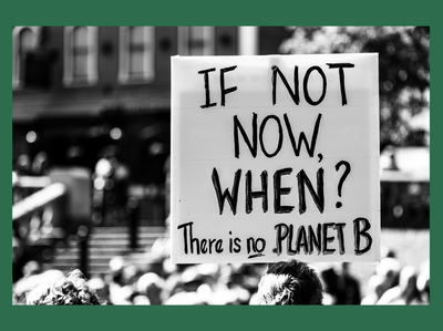 black and white photo at a climate protest with a poster/sign that reads "if not now, when? there is no planet B"