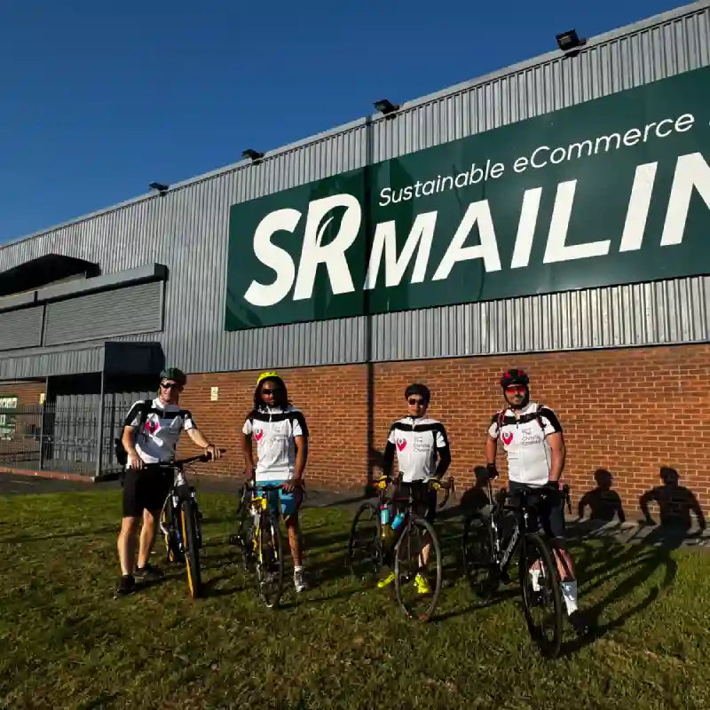 Group of cyclists in front of a building with 'SR MAILING' branding