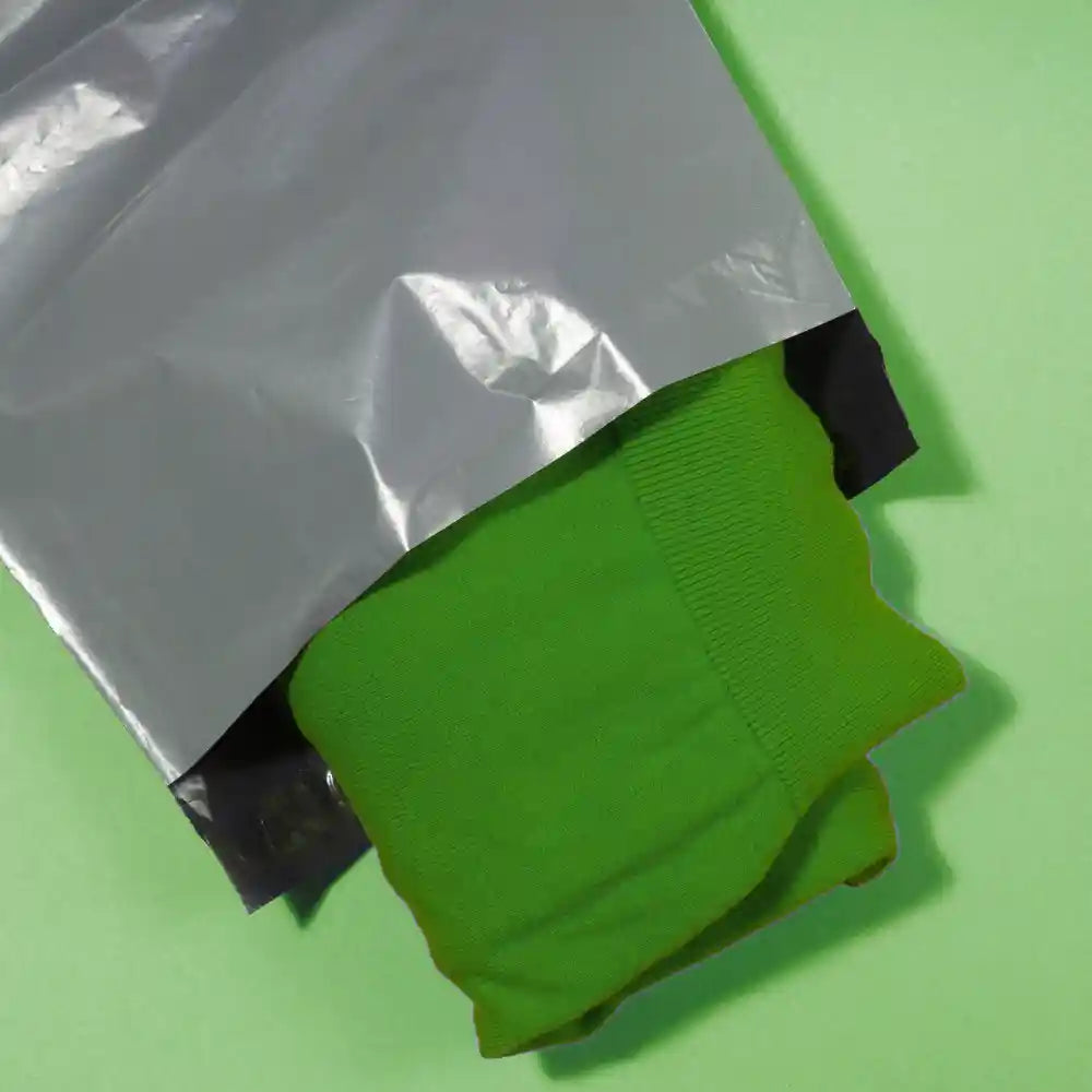 Green jumper inside recycled mailing bag on green background
